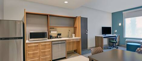 A modern kitchen with a built-in microwave, refrigerator, and dishwasher. There is a dining area with a table and chairs, and a small office space with a desk and computer.