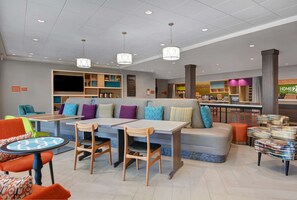 A modern hotel lobby with seating areas, a bar, and a children's play area. - Home2 Suites by Hilton Panama City Beach, FL (Panama City Beach)