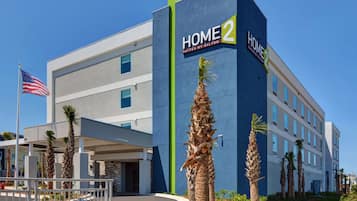 A modern hotel with a prominent 'HOME 2' sign, featuring a two-story structure with a flat roof and a covered entrance area.