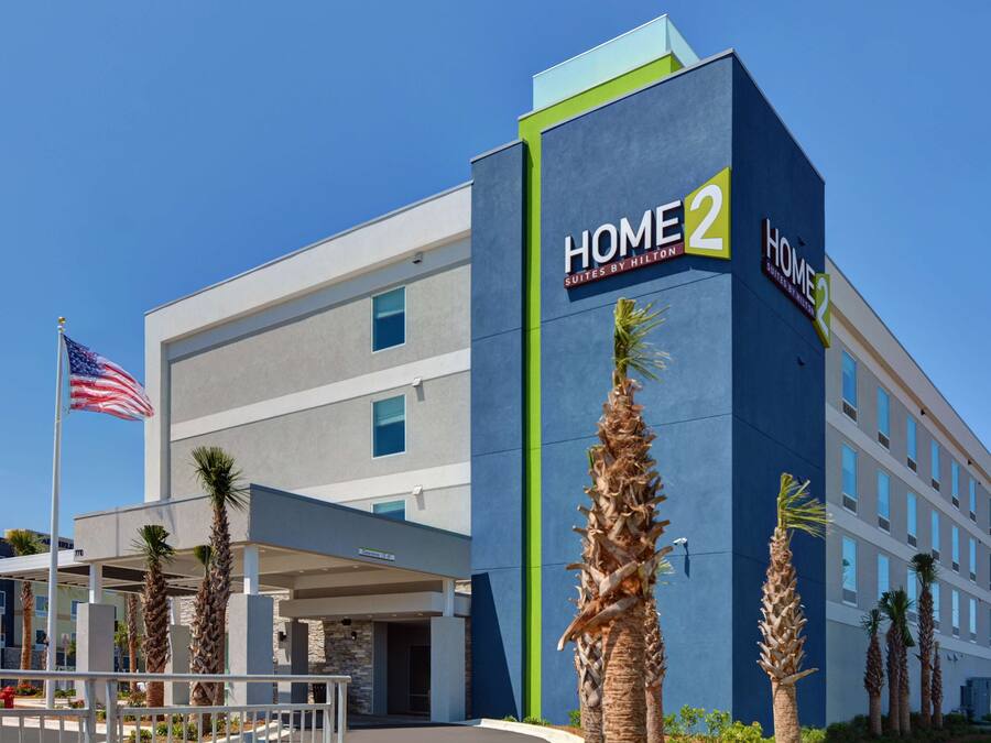 A modern hotel with a prominent 'HOME 2' sign, featuring a two-story structure with a flat roof and a covered entrance area.