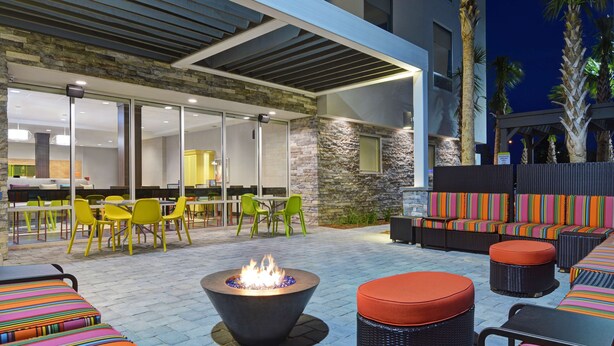 An outdoor seating area with a fire pit, wicker furniture, and a stone wall. - Home2 Suites by Hilton Panama City Beach, FL (Panama City Beach)