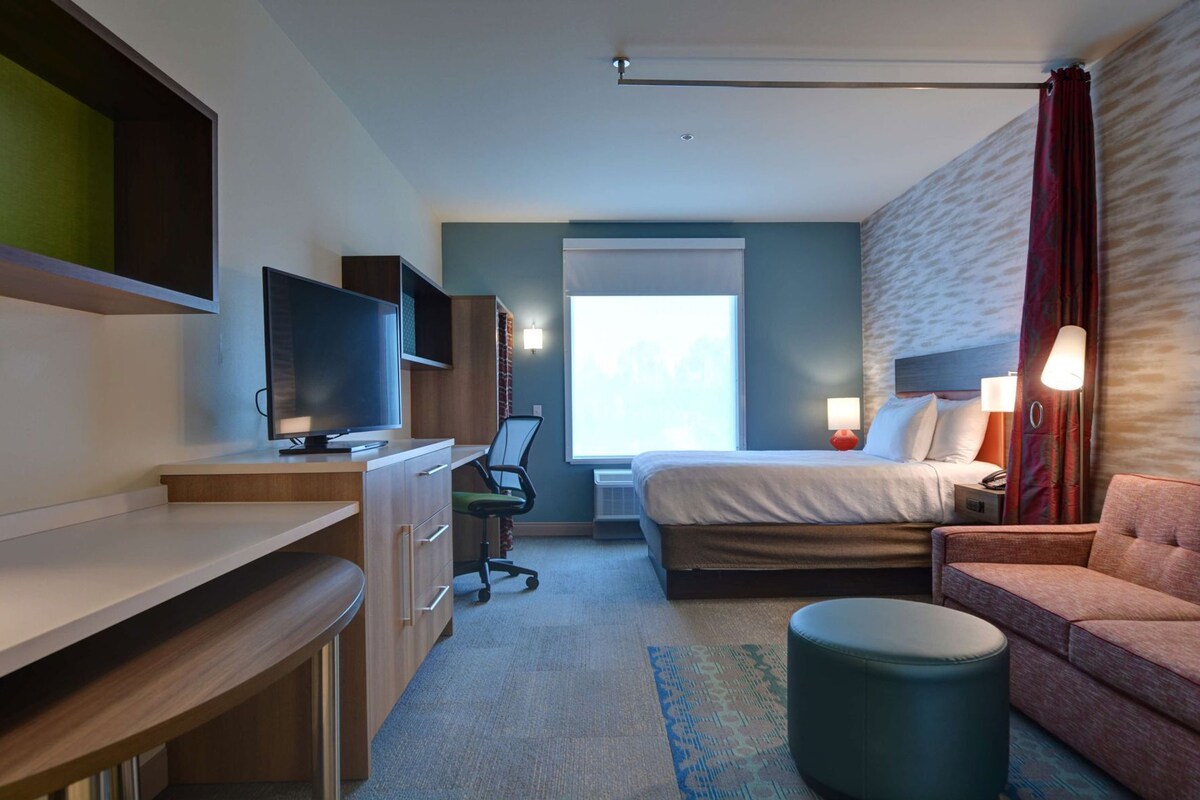 A hotel room with a bed, a desk with a computer, a chair, a couch, and a small ottoman.
