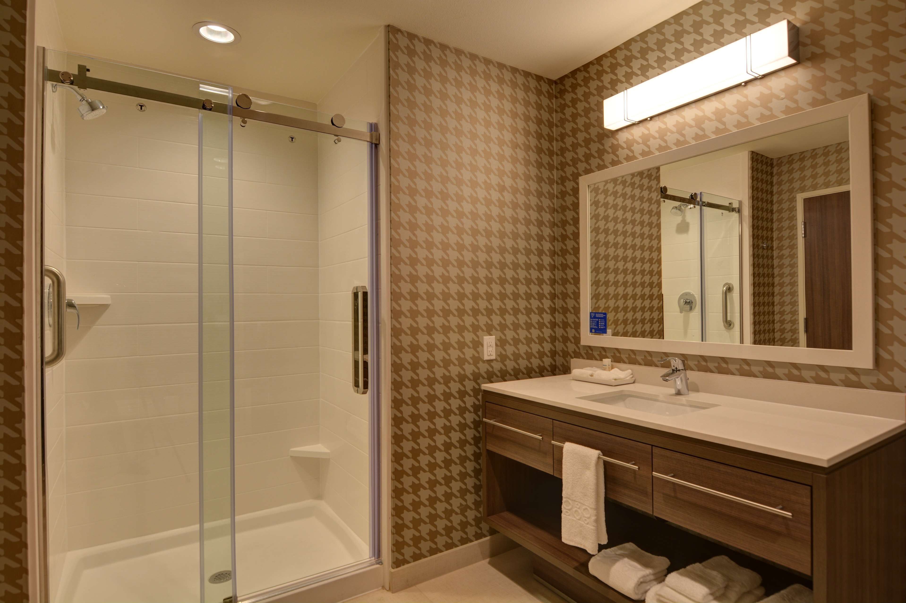 A bathroom with a glass-enclosed shower, a vanity with a mirror, and patterned wall tiles.