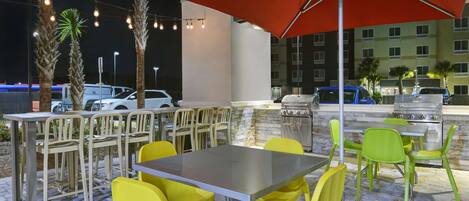 An outdoor patio area with a table and chairs, a grill, and a red umbrella.