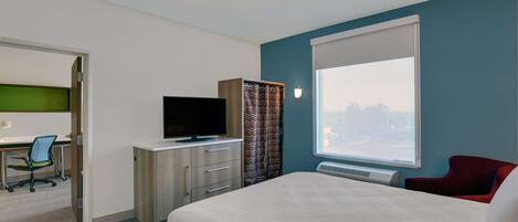 A hotel room with a bed, a desk with a chair, a television, and a window with curtains.