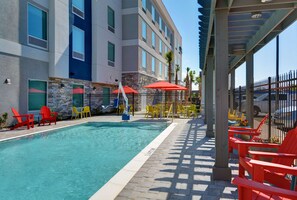A swimming pool with red and yellow chairs, a covered seating area, and a building with stone and blue accents. - Home2 Suites by Hilton Panama City Beach, FL (Panama City Beach)