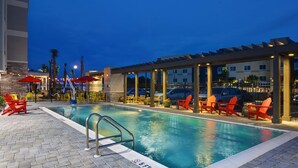 A swimming pool with red chairs and umbrellas, surrounded by a covered area with a pergola. - Home2 Suites by Hilton Panama City Beach, FL (Panama City Beach)