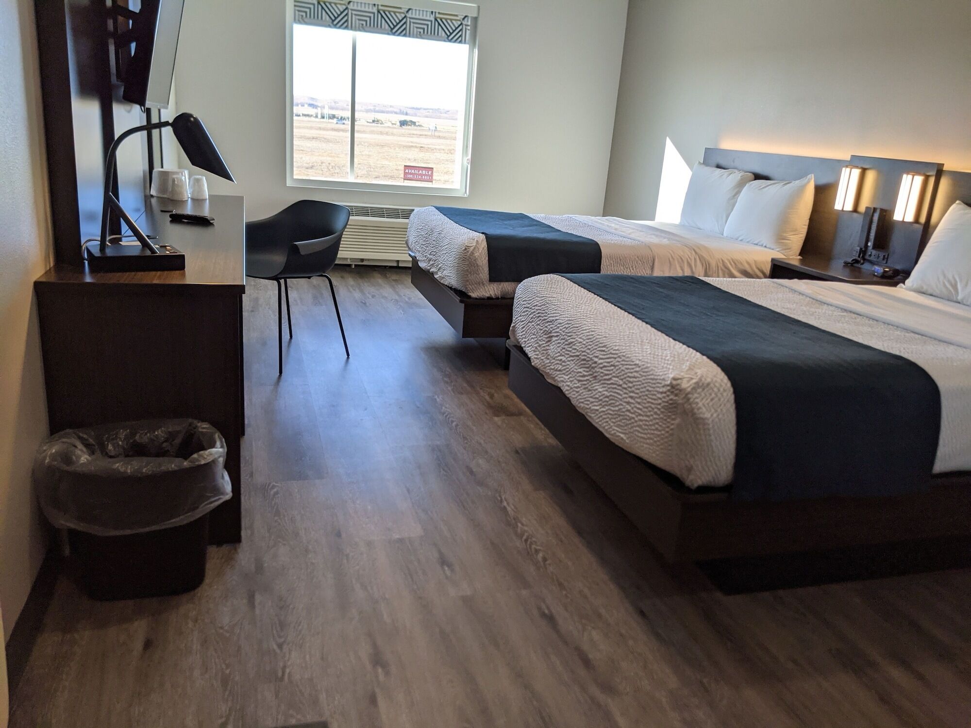 Habitación de hotel con dos camas, un escritorio, una silla y vistas al exterior.