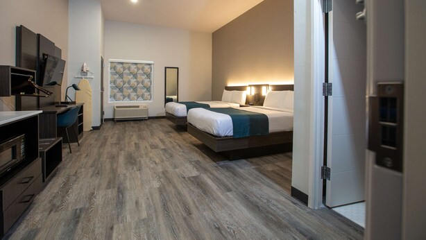 Ein Hotelzimmer mit Küchenzeile, einem Bett mit Kopfteil, einem Schreibtisch mit Stuhl und einem großen Spiegel.