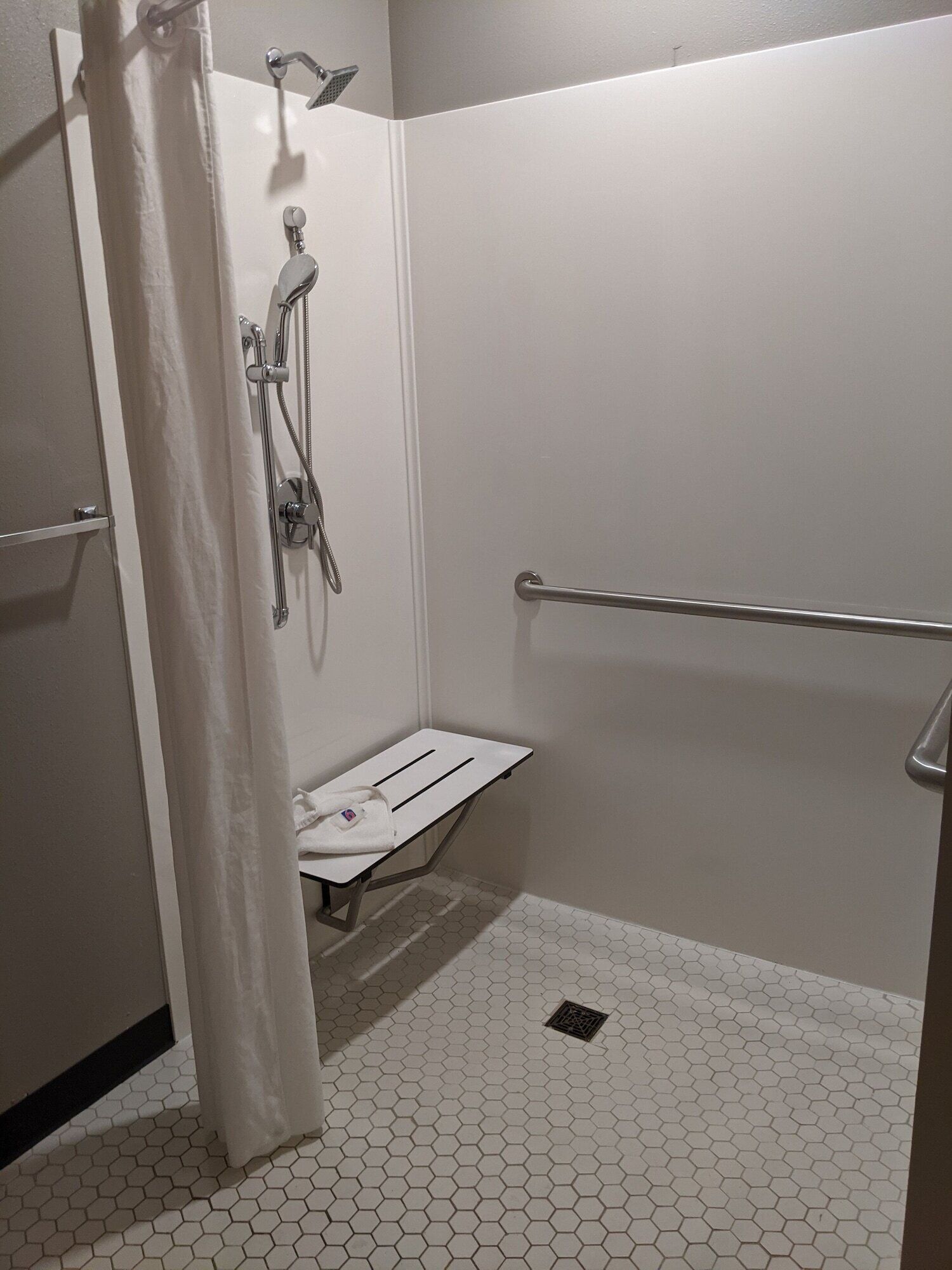 A small, enclosed shower area with a white showerhead, a handheld showerhead, and a towel rack.