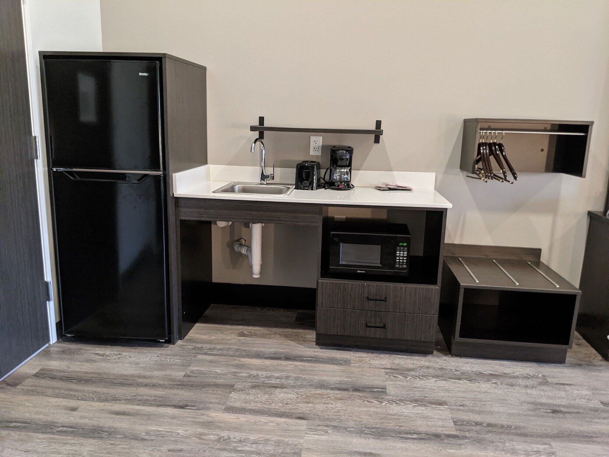 Una cocina compacta con un refrigerador negro, un microondas, una cafetera y un mueble pequeño.