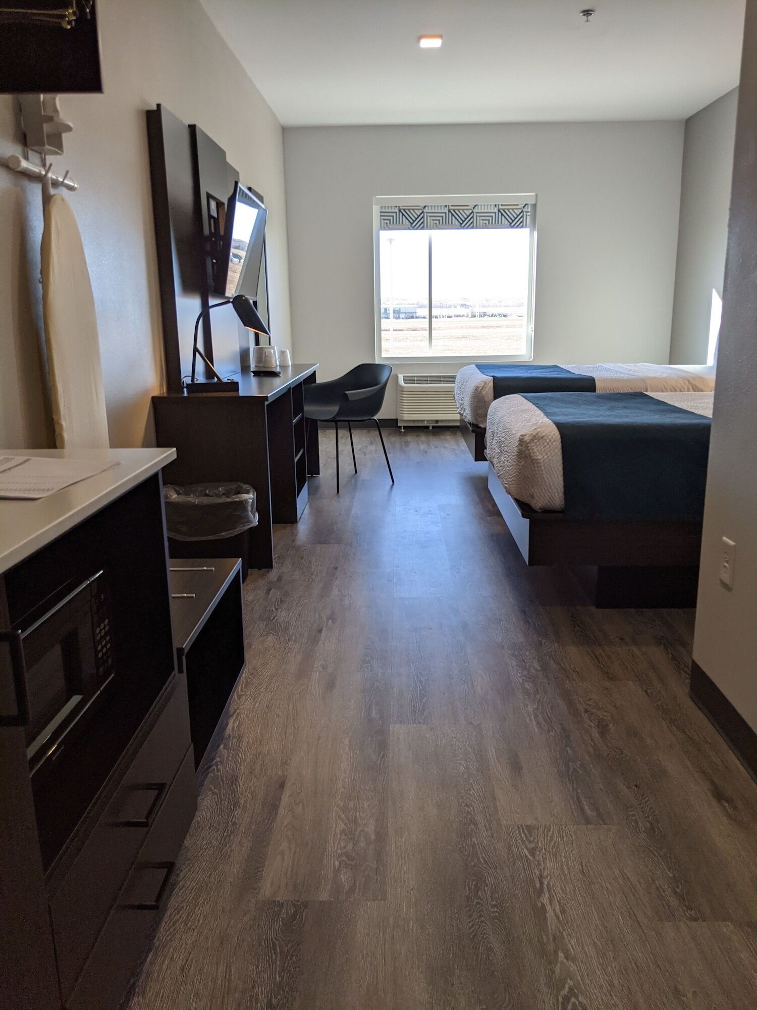 A modern hotel room with a wooden floor, a desk with a chair, a bed, a TV, and a window with a view of the outside.