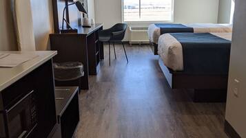A modern hotel room with a wooden floor, a desk with a chair, a bed, a TV, and a window with a view of the outside.