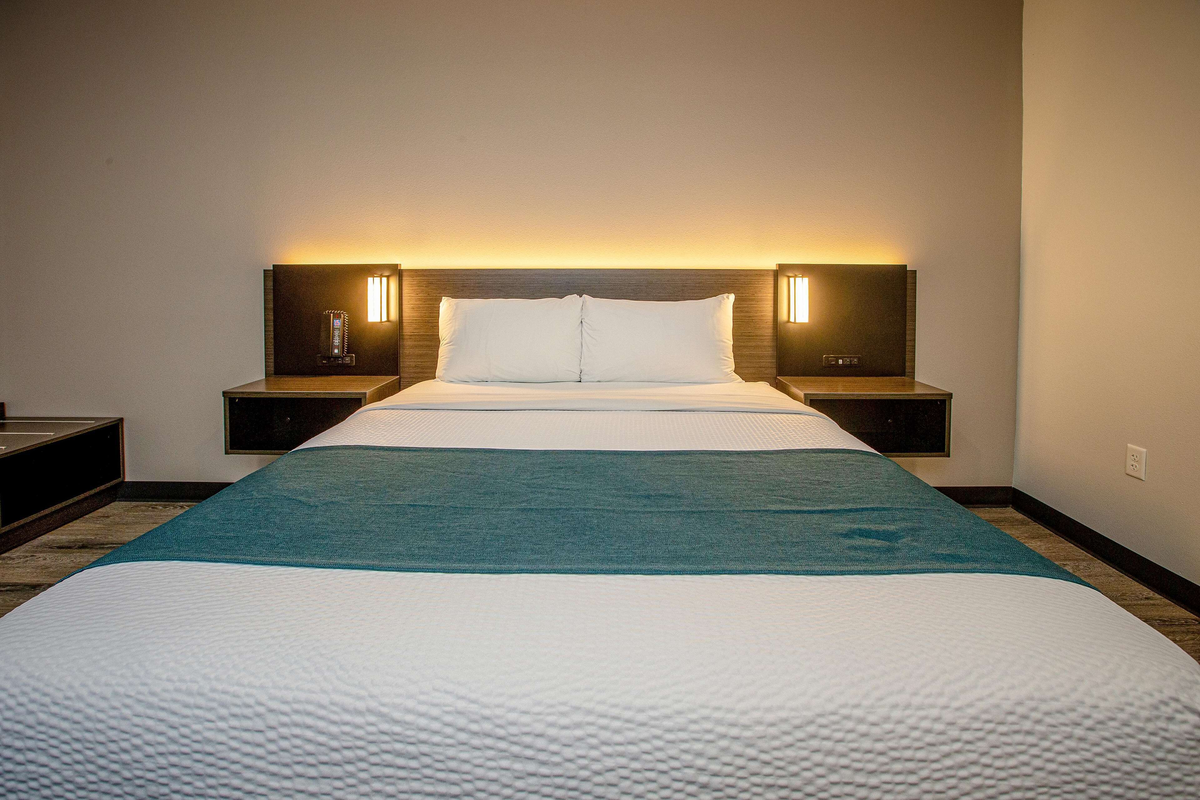 Una habitación de hotel con una cama grande, dos mesitas de noche y un cabecero con iluminación integrada.