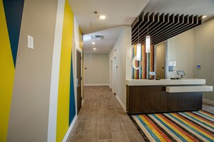 Un área de recepción moderna con un mostrador de madera, un colorido tapete a rayas y una lámpara fijada a la pared.