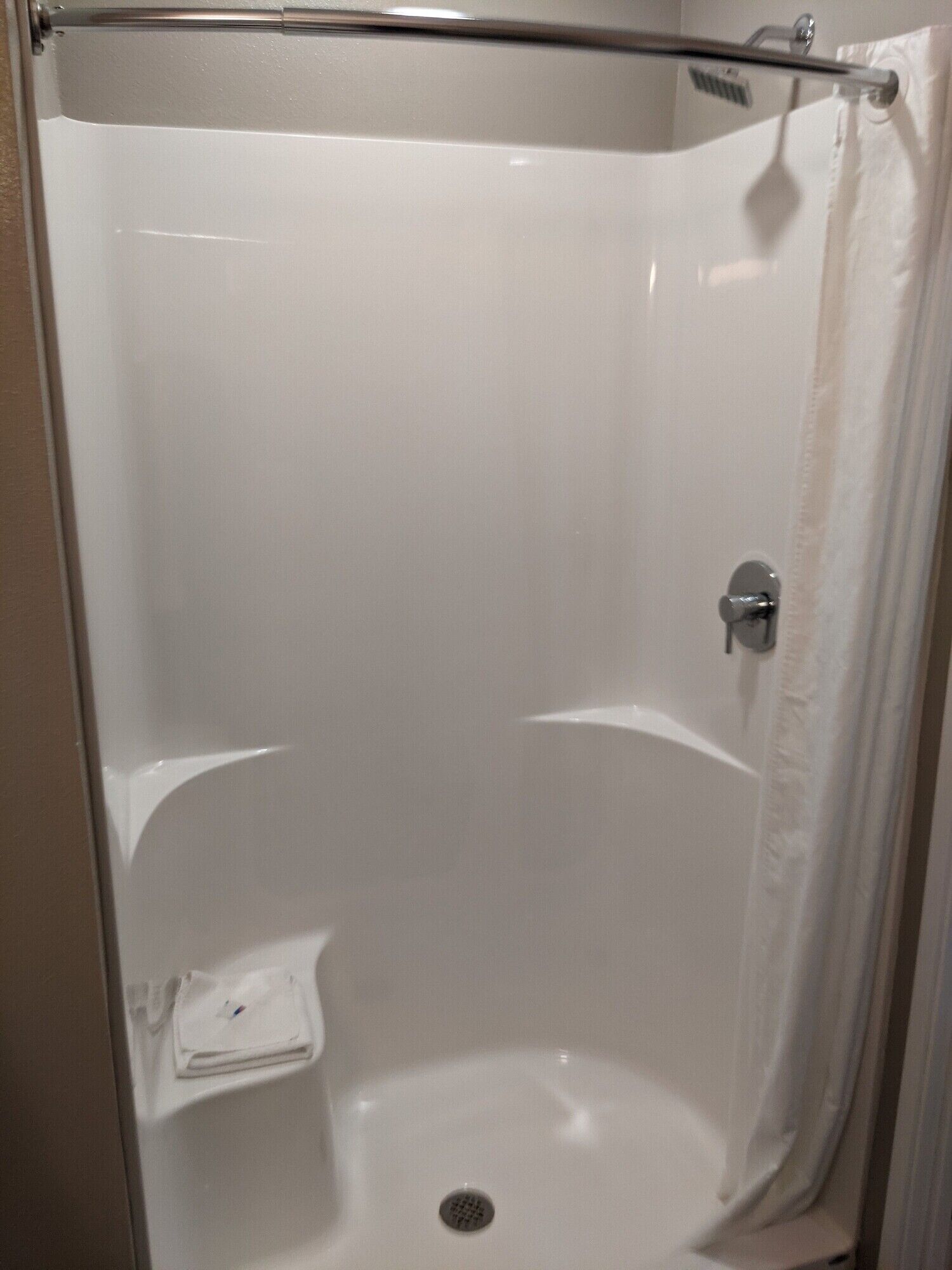 A small, enclosed shower stall with a white interior, a shower curtain, and a small shelf.