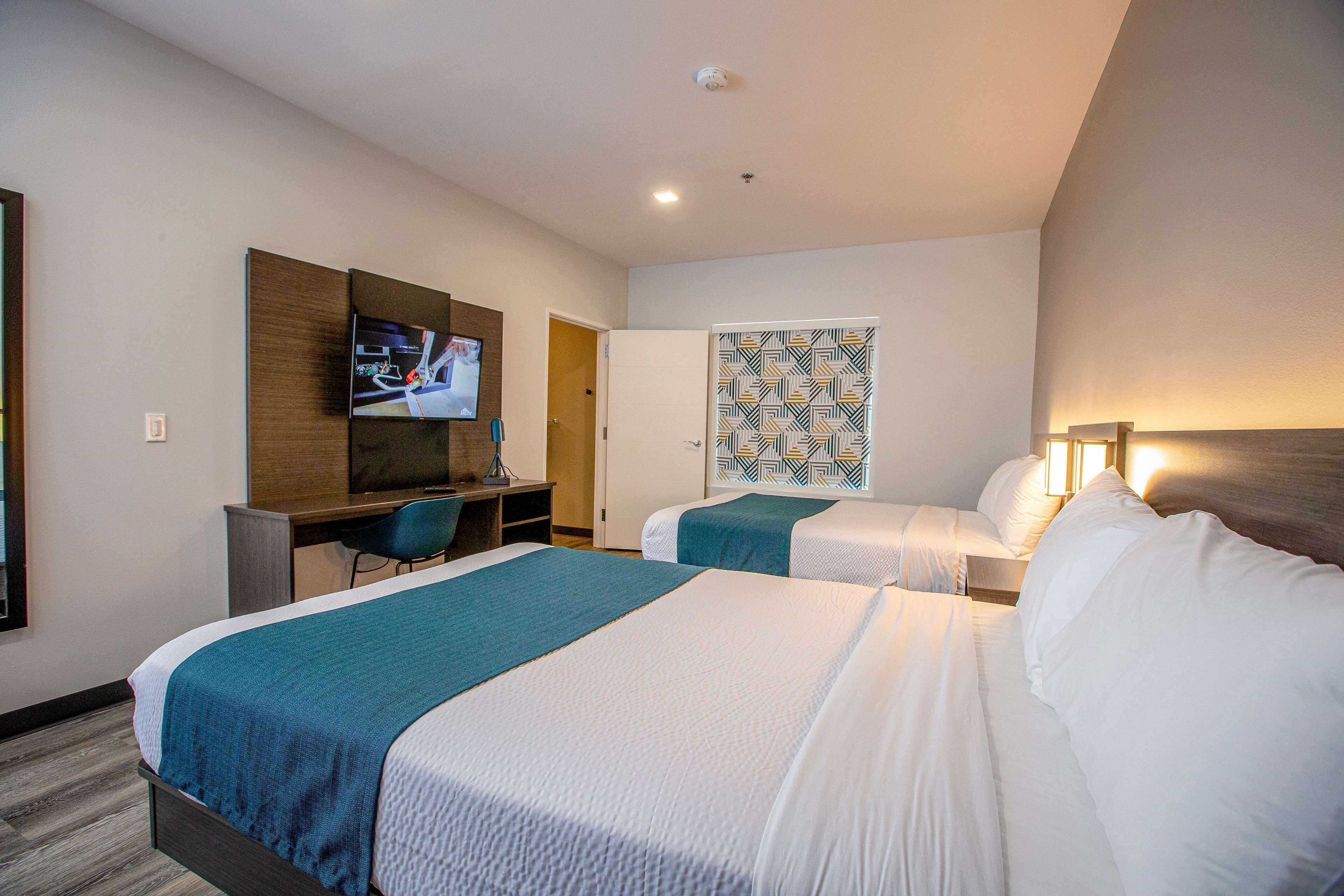 Habitación de hotel con dos camas, un escritorio, un televisor y una pared con diseño.