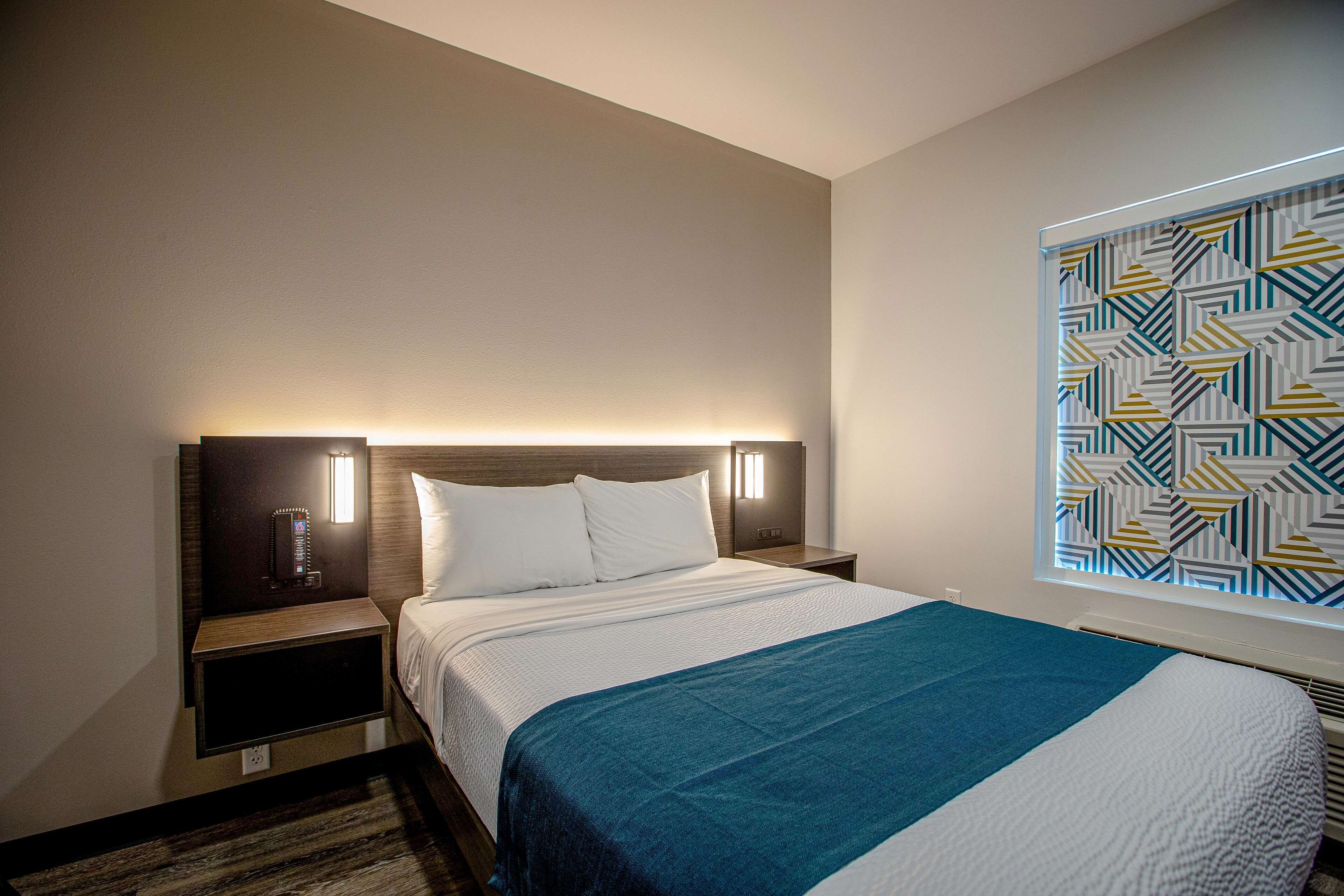 A hotel room with a large bed, a nightstand with a lamp, and a wall-mounted TV.