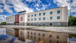 A multi-story hotel with a prominent '6' sign, a parking lot, and a reflective wet surface. - Motel 6 North Platte, NE - East (North Platte)