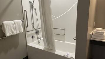 Un baño moderno con bañera, ducha y barras de apoyo. Hay toallas en un perchero y una repisa.