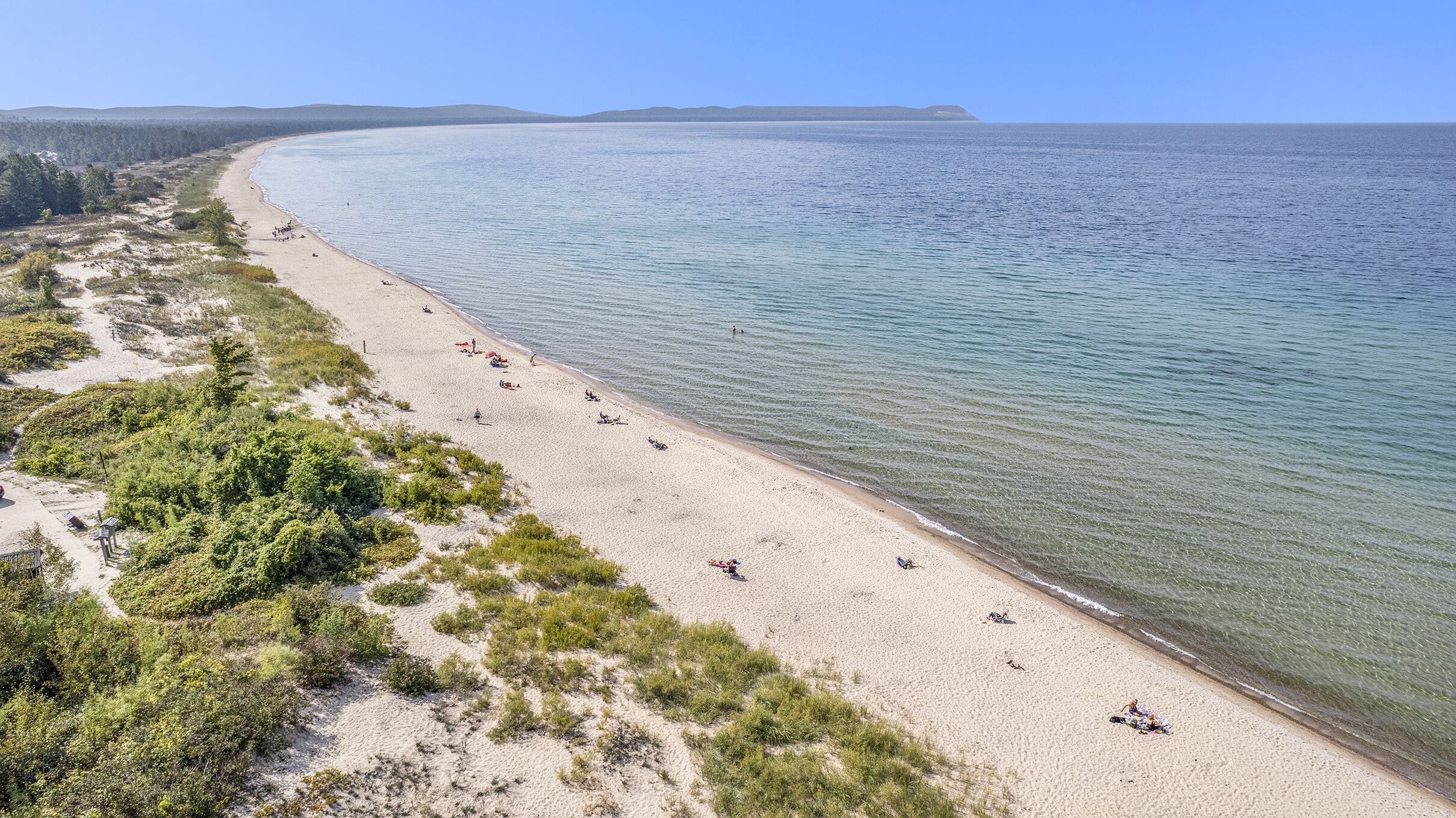 Een strand met helder water, een zandstrand en weinig begroeiing.