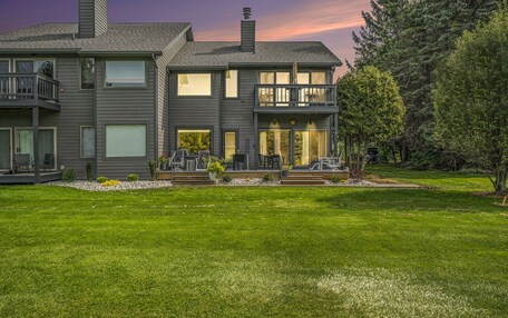 A two-story house with a balcony, a well-maintained lawn, and a large window.