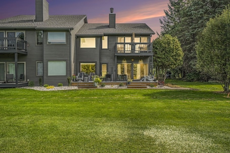 A two-story house with a balcony, a well-maintained lawn, and a large window.