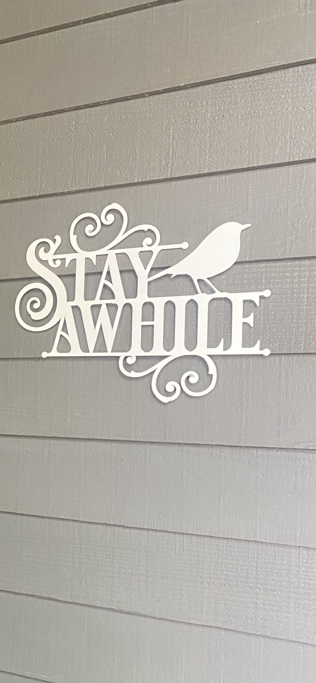 A decorative sign with the phrase "Stay Awhile" and a bird silhouette.