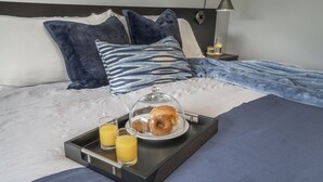 Een net opgemaakt bed met een ontbijttafel, inclusief een croissant, twee glazen sinaasappelsap en een glas melk.