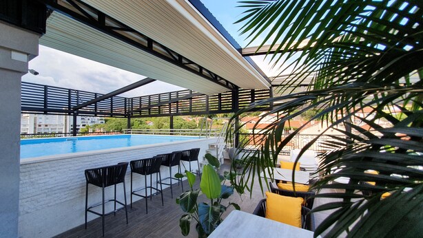 A rooftop pool area with a view of the cityscape, a covered seating area, and a security camera. - Hotel Pasha (Mostar)