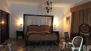 Un dormitorio con una cama grande, dos mesitas de noche, una araña, una silla y una mesa redonda.