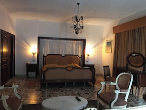 Un dormitorio con una cama grande, dos mesitas de noche, una araña, una silla y una mesa redonda.