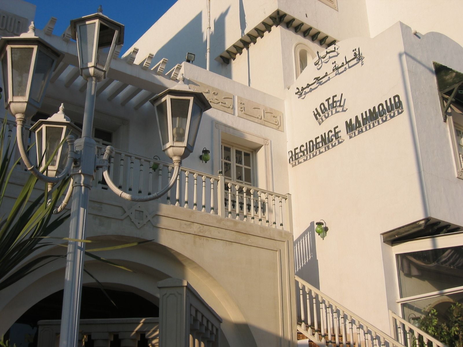Un edificio blanco con un balcón, una farola y un cartel que dice 'Hotel Residence Mahmoud'.