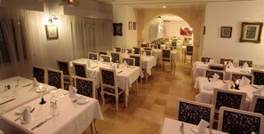 A formal dining room with multiple tables and chairs, arranged in rows, with a chandelier and wall-mounted lights. - Hotel Residence Mahmoud (Hammamet)