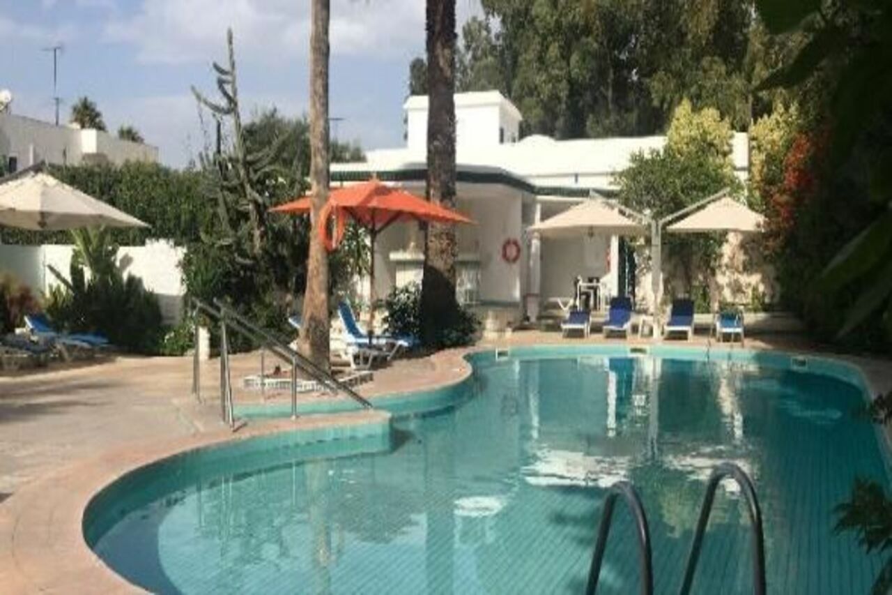 A swimming pool with lounge chairs and umbrellas, surrounded by trees and a building.