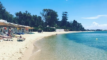 A beach with clear water, umbrellas, and beach chairs.