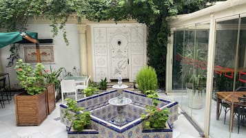 A courtyard with a tiled fountain, seating area, and potted plants.