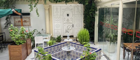 A courtyard with a tiled fountain, seating area, and potted plants.