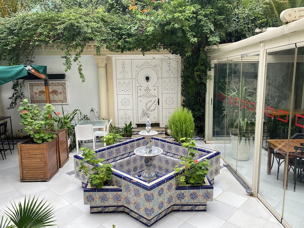 Un patio con una fuente de azulejos, zona de estar y plantas en macetas.