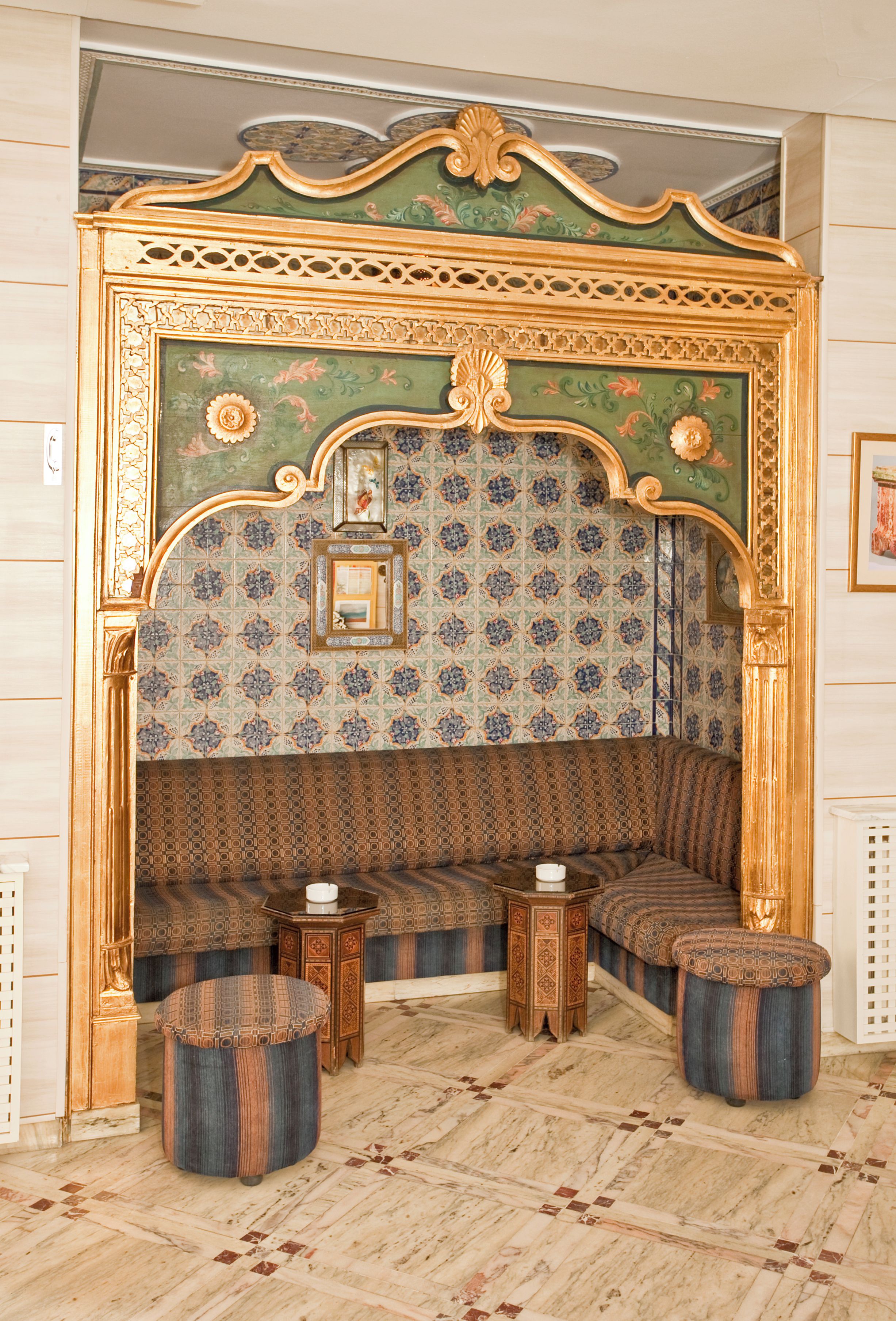 A room with a patterned wall, a sofa, a small table, and two stools.