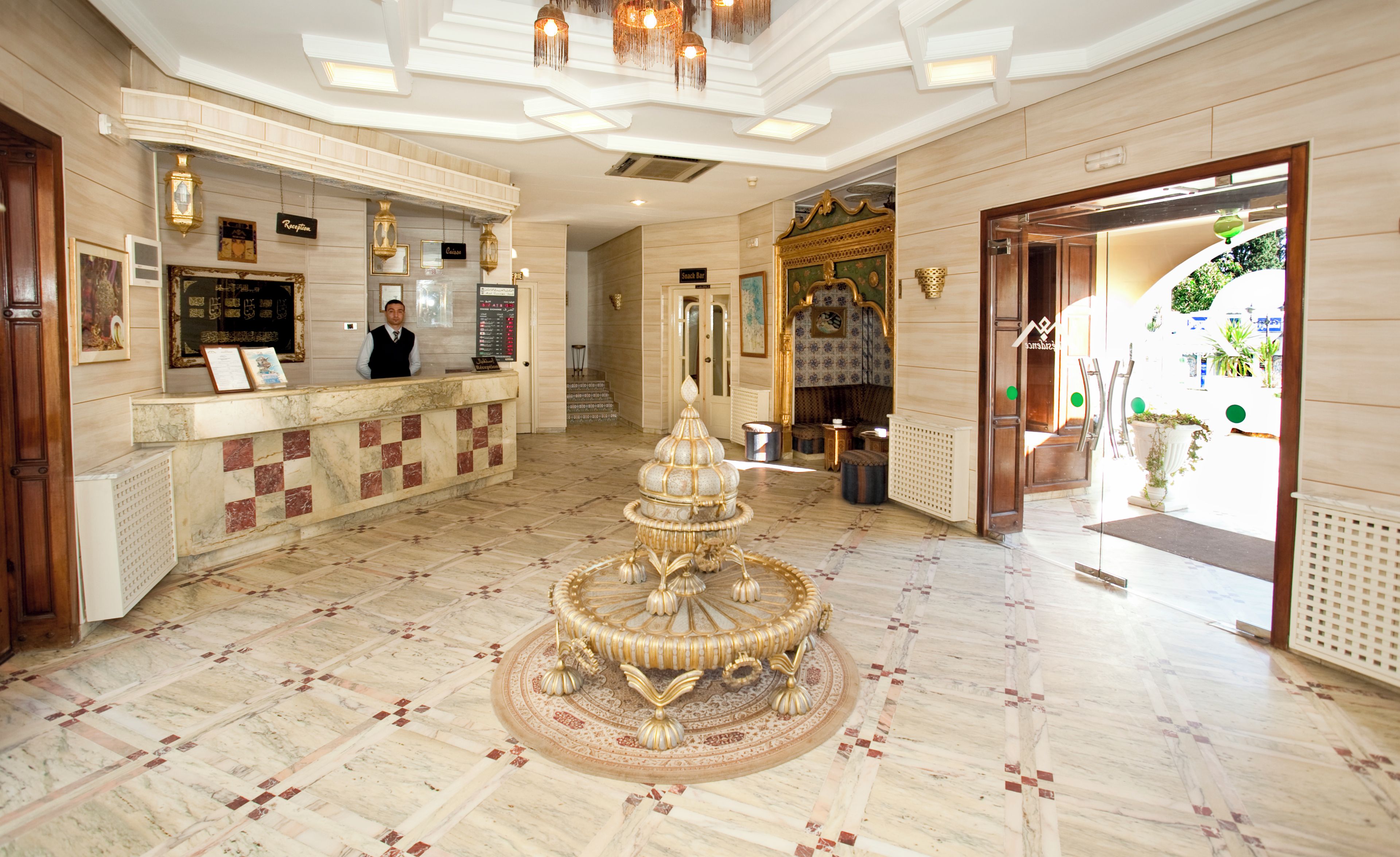 A lobby with a reception desk, a decorative fountain, and a staircase leading to an upper floor.