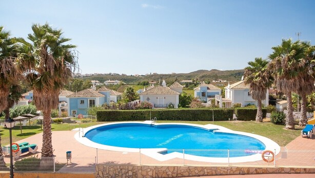 A swimming pool surrounded by palm trees and houses with tiled roofs. - Villas del Golf TH 23 (Manilva)