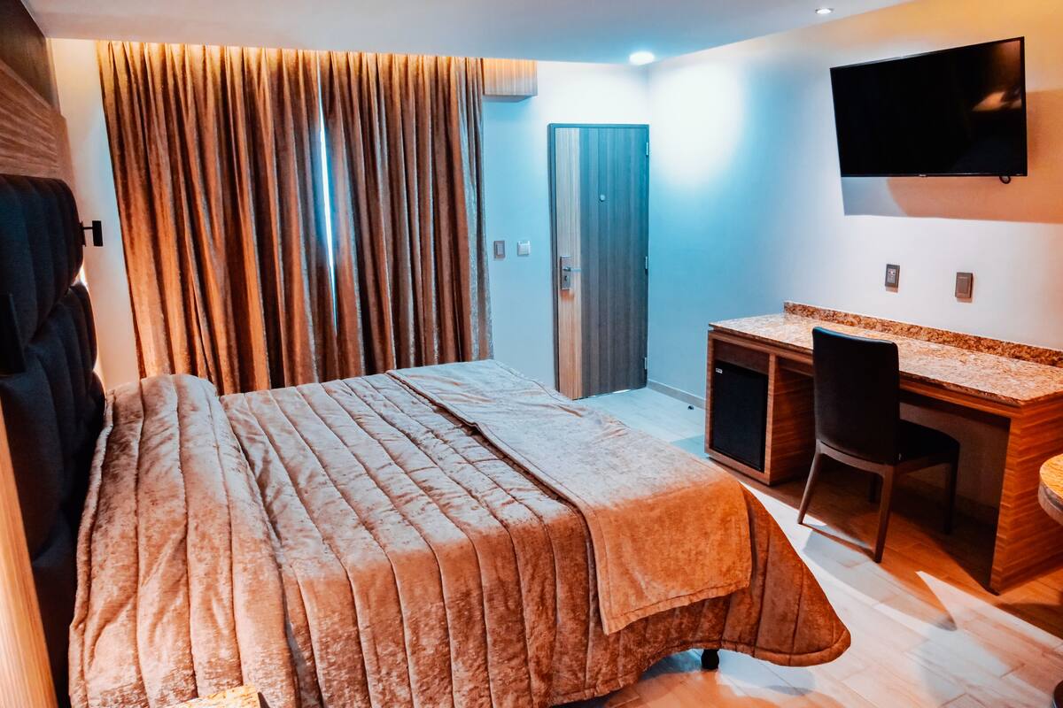 Habitación de hotel con cama, escritorio, silla, televisor y puerta.
