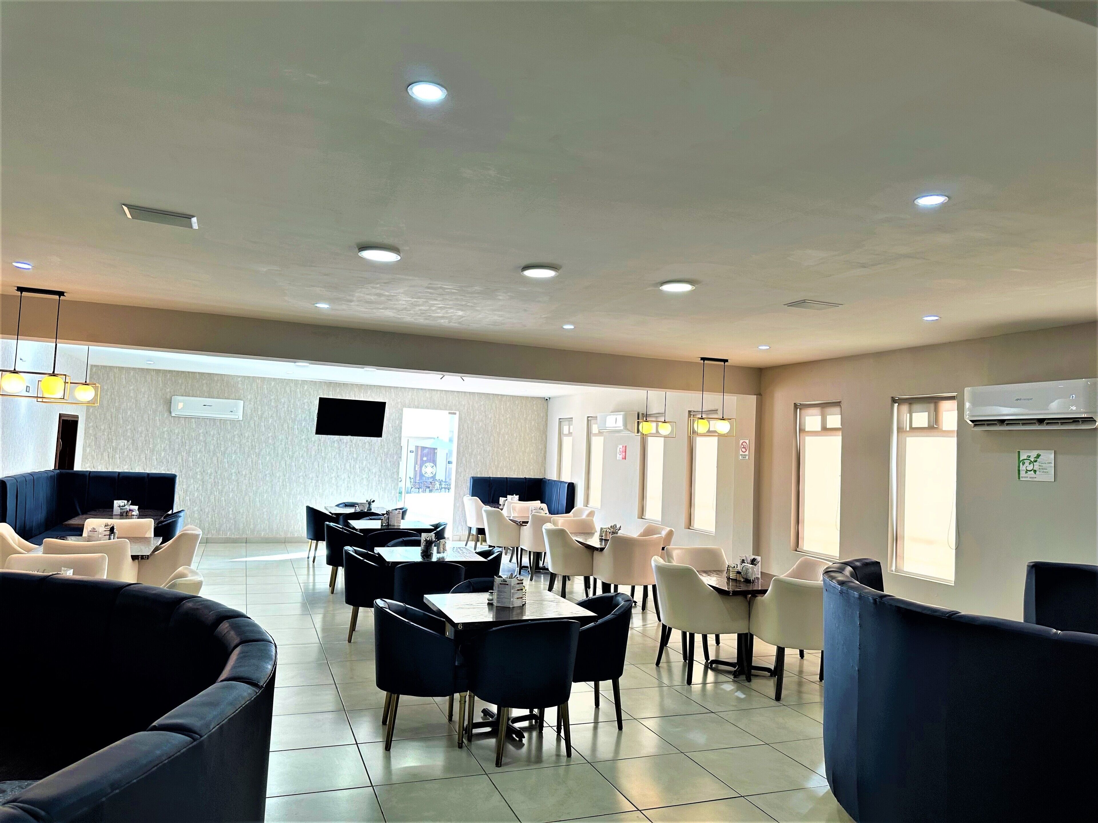 A spacious dining area with multiple tables and chairs, recessed ceiling lights, and a flat-screen TV mounted on the wall.
