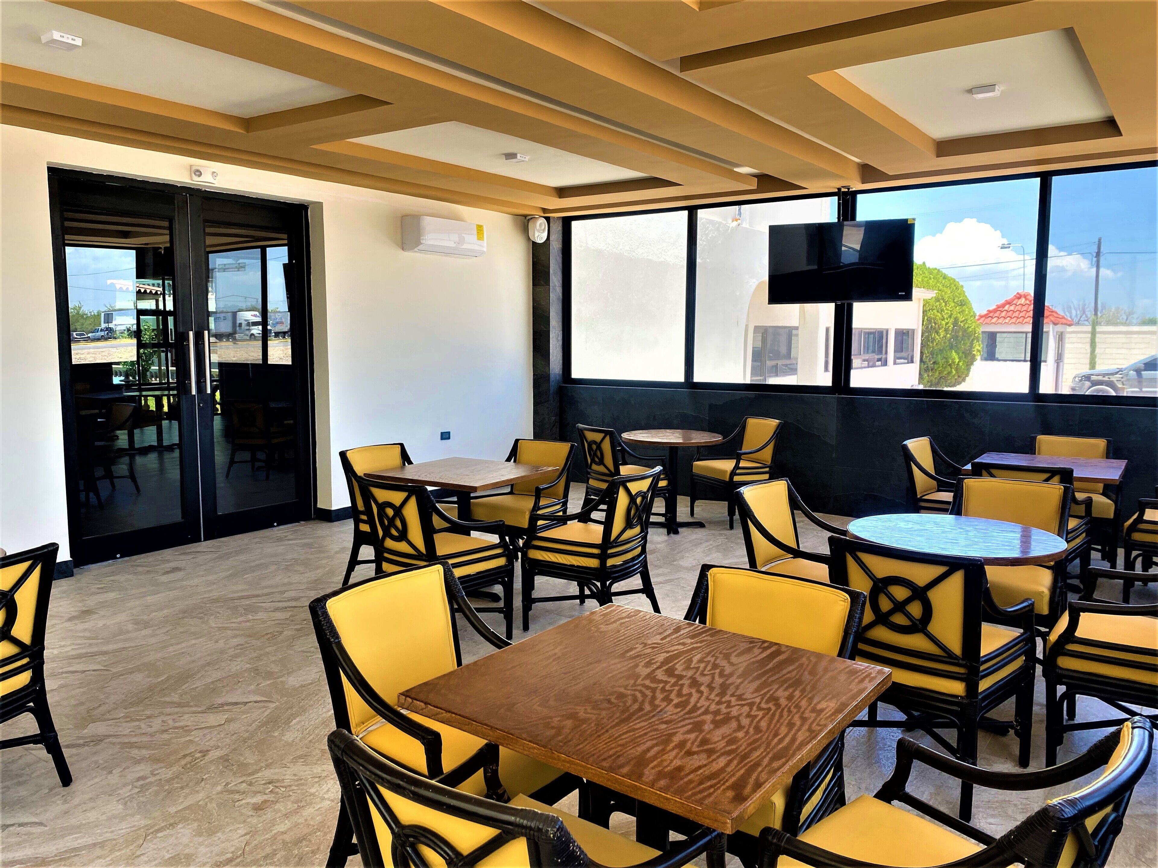A restaurant with yellow chairs and tables, large windows, and a flat-screen TV.