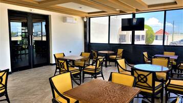 A restaurant with yellow chairs and tables, large windows, and a flat-screen TV.