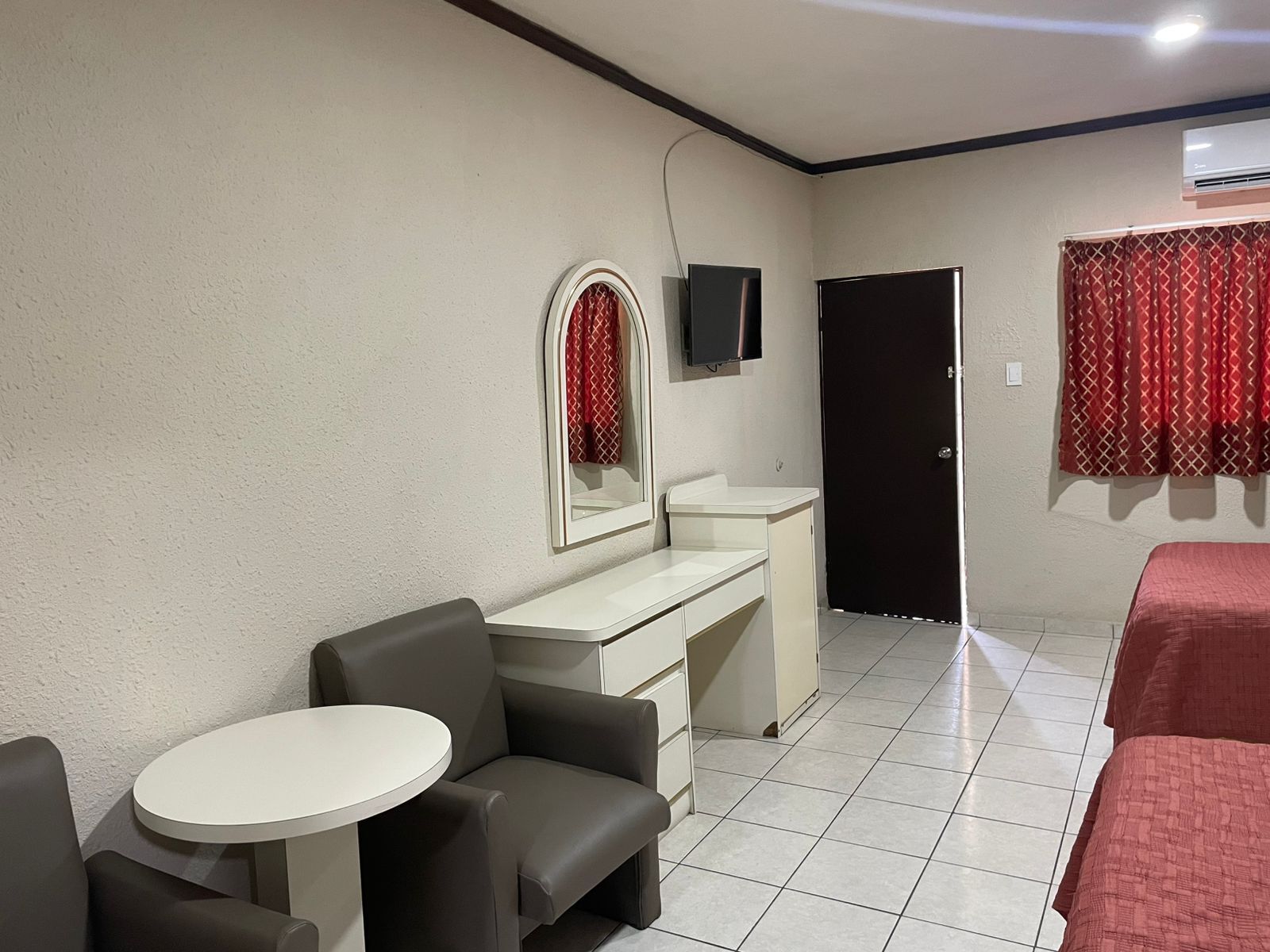 A hotel room with a bed, a desk with a chair, a small round table, and a TV mounted on the wall.