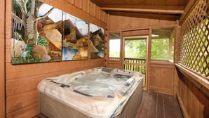 A wooden cabin with a hot tub, wooden walls, and a view of greenery outside.