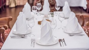 A dining table set with white tablecloths, plates, and cutlery.