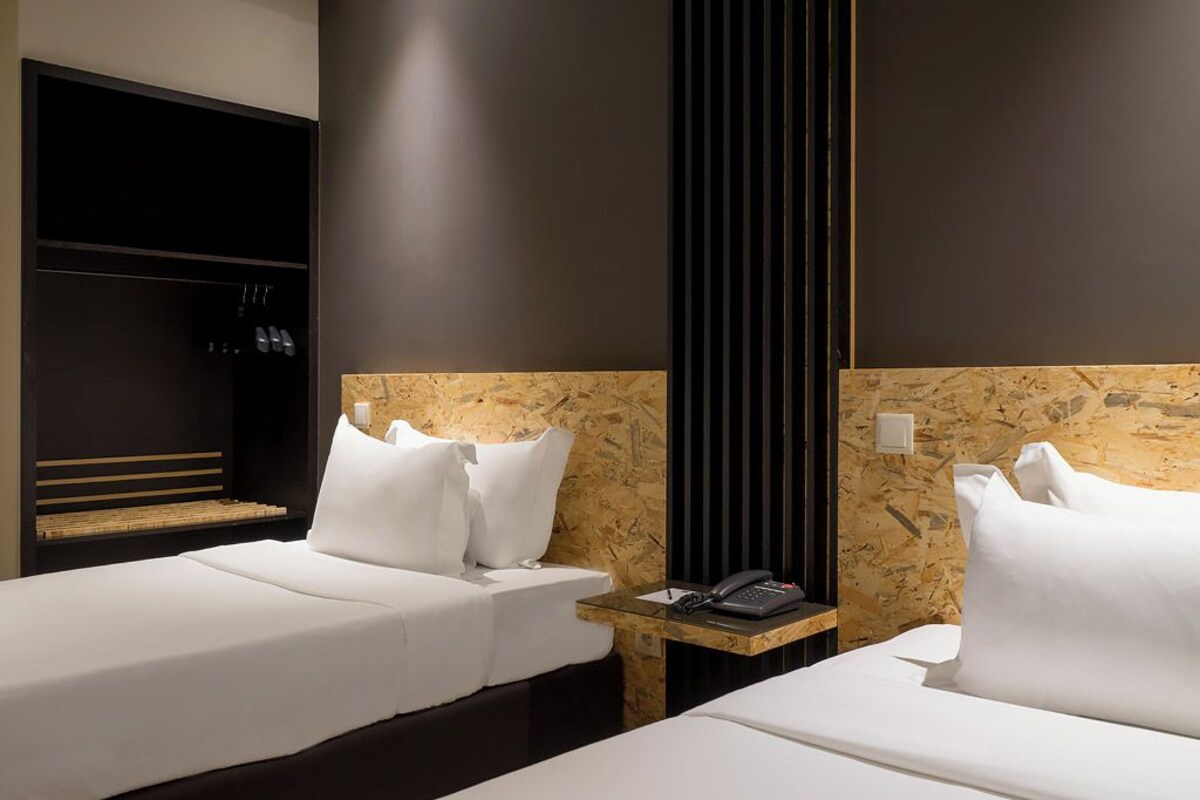 A hotel room with two beds, a wooden headboard, a bedside table with a phone, and a wardrobe.